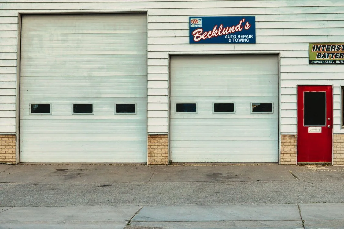 Auto repair shop exterior with two roll-up service bay doors and a red entrance door