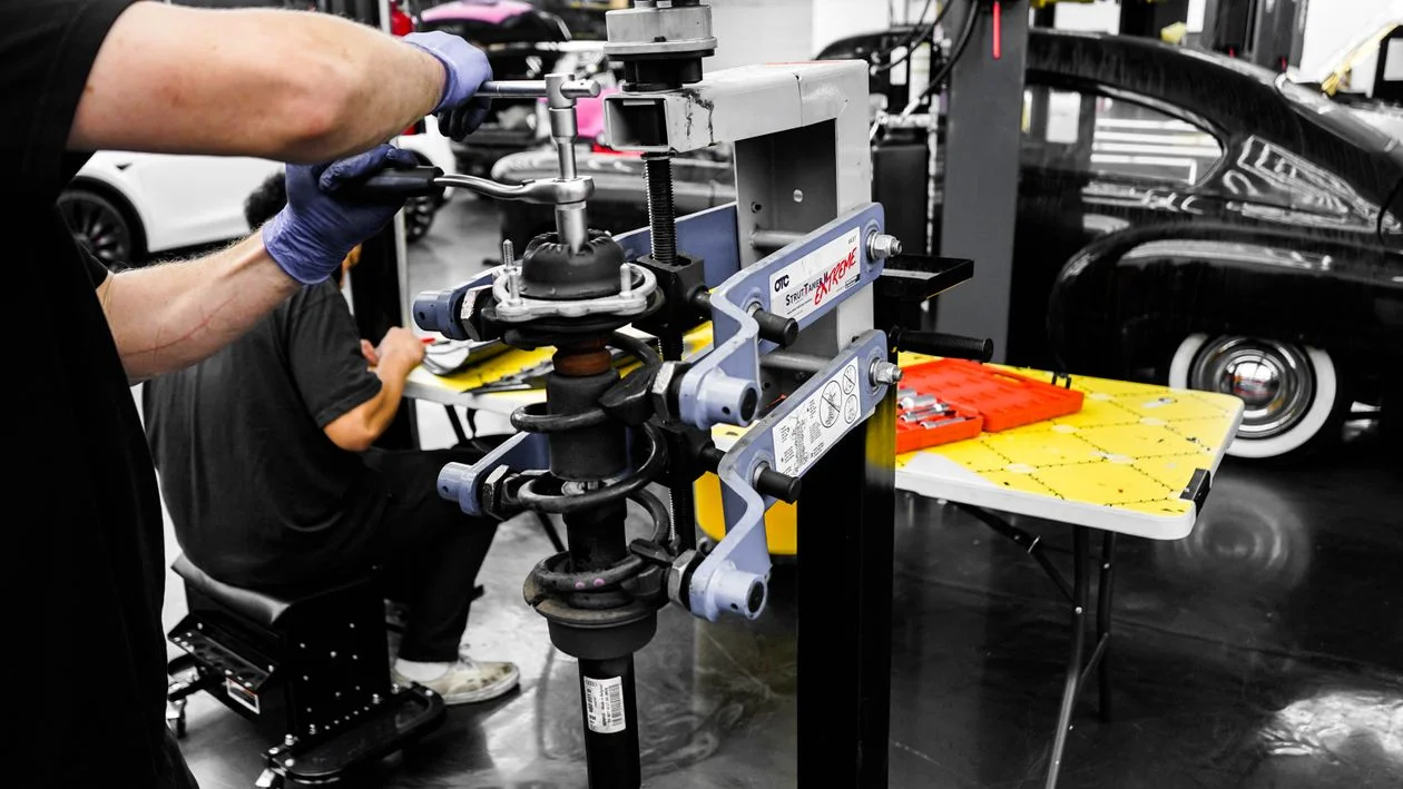 Technician using a strut spring compressor in an auto repair workshop